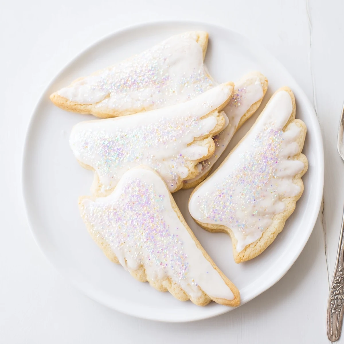 Plate of Angel Wings sugar cookies, beautifully iced and dusted with sparkling sugar.