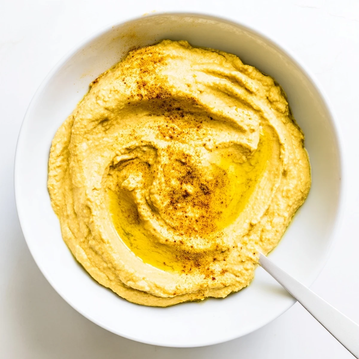 A smooth, golden bowl of chickpea curry paste garnished with olive oil drizzle and curry powder.