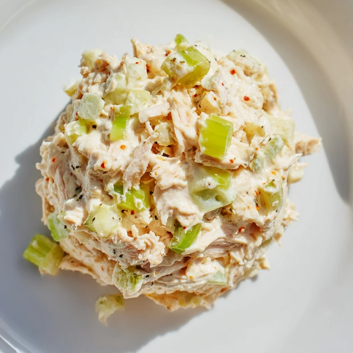 Spicy Zesty Tuna Salad with flaky tuna and fresh scallions sits in a white bowl on a rustic wooden table.