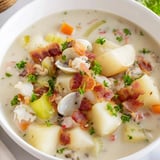 Freshly garnished New England Clam Chowder, showcasing a rich, thick, and flavorful seafood soup.