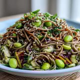 Freshly cooked soba noodles topped with colorful vegetables and toasted sesame seeds in a rustic ceramic bowl.