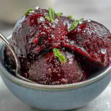 A scoop of homemade Black Currant Sorbet in a chilled glass, showcasing its deep purple hue and smooth, icy texture.