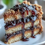 Golden PB and J Cake slices on a white plate with a pitcher of luscious black currant sauce nearby. 
