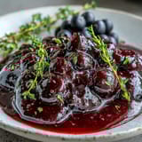 Warm Black Currant Reduction simmering in a saucepan, showing dark glossy texture and steam rising from the mixture.
