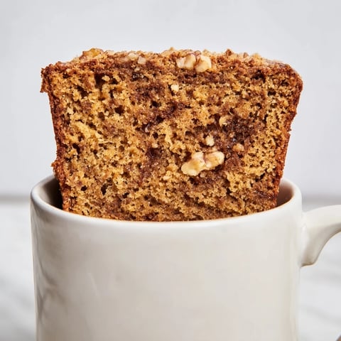Warm pumpkin bread in a mug, golden-brown and inviting with a sprinkle of walnuts.