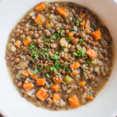 Steaming bowl of Lentil Soup with carrots and celery, garnished with fresh herbs, ready to serve.