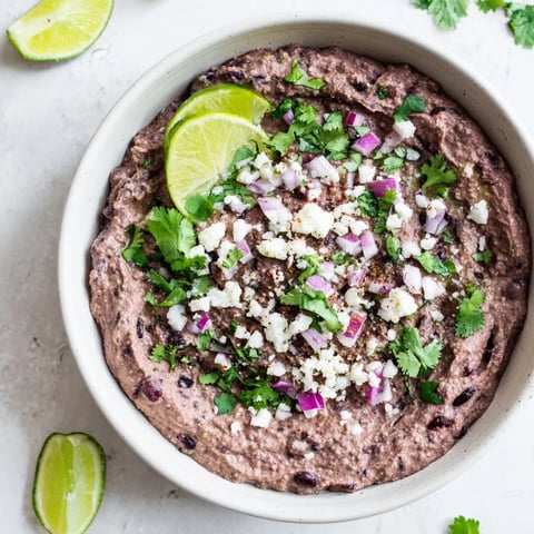 A close-up of Spicy Black Bean Dip in a rustic bowl, garnished with fresh cilantro, sliced jalapeños, and lime wedges for a vibrant party appetizer.