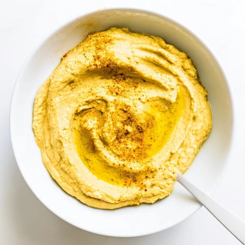 A smooth, golden bowl of chickpea curry paste garnished with olive oil drizzle and curry powder.