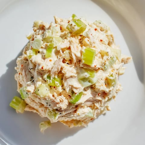 Spicy Zesty Tuna Salad with flaky tuna and fresh scallions sits in a white bowl on a rustic wooden table.