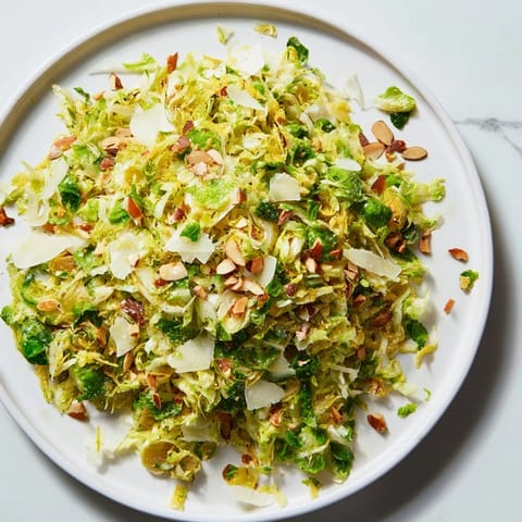 Fresh Crunchy Lemon Parmesan Brussels Sprouts Salad, topped with toasted almonds and grated Parmesan for serving.