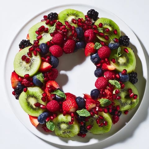 Vibrant fruit plate holiday wreath of kiwi, berries, and mint, a colorful appetizer ideal for festive events.