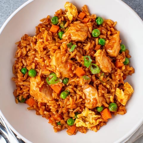 A close-up of butter chicken fried rice garnished with green onions, showcasing a colorful and hearty meal for four.