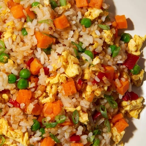 A close-up view of golden Egg Fried Rice with peas, carrots, and scallions, garnished with a fresh lime wedge on a rustic plate.