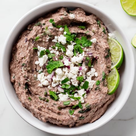 Creamy Spicy Black Bean Dip served with crunchy tortilla chips and colorful vegetable sticks, perfect for game day snacks or taco night spreads.