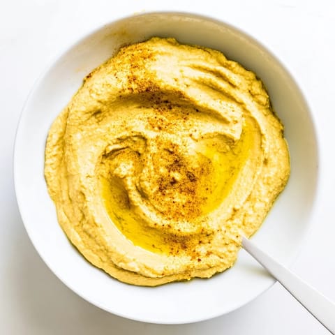 A smooth, golden bowl of chickpea curry paste garnished with olive oil drizzle and curry powder.