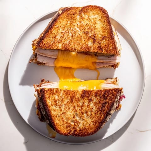 A close-up of a golden-brown Smoked Turkey Grilled Cheese, oozing with sharp cheddar and tangy cranberry spread on sourdough bread.