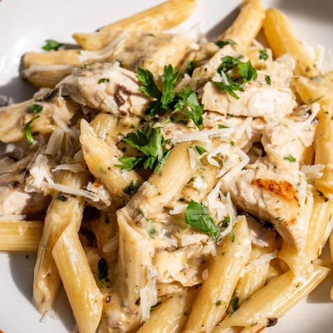 An overhead shot of Roasted Garlic Chicken Penne, showcasing the silky roasted garlic cream sauce clinging to each pasta tube and golden chicken piece.  