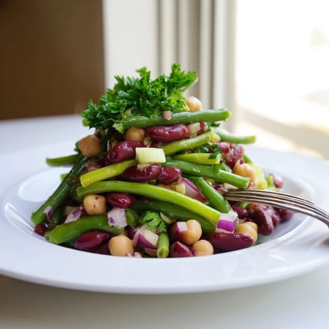 Brightly colored Three-Bean Salad in a glass bowl, featuring green beans, red kidney beans, and chickpeas tossed with fresh parsley and red onion.  