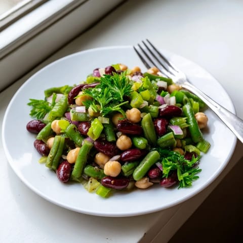 A close-up of vibrant Three-Bean Salad, glistening with tangy apple cider vinaigrette and dotted with crisp celery slices on a rustic wooden table.  