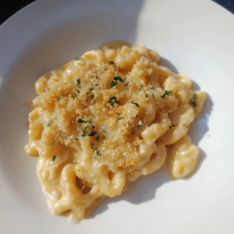 A close-up of a bubbling Lightened Mac & Cheese Snowflake Pasta Bake with melted cheese and fresh parsley.