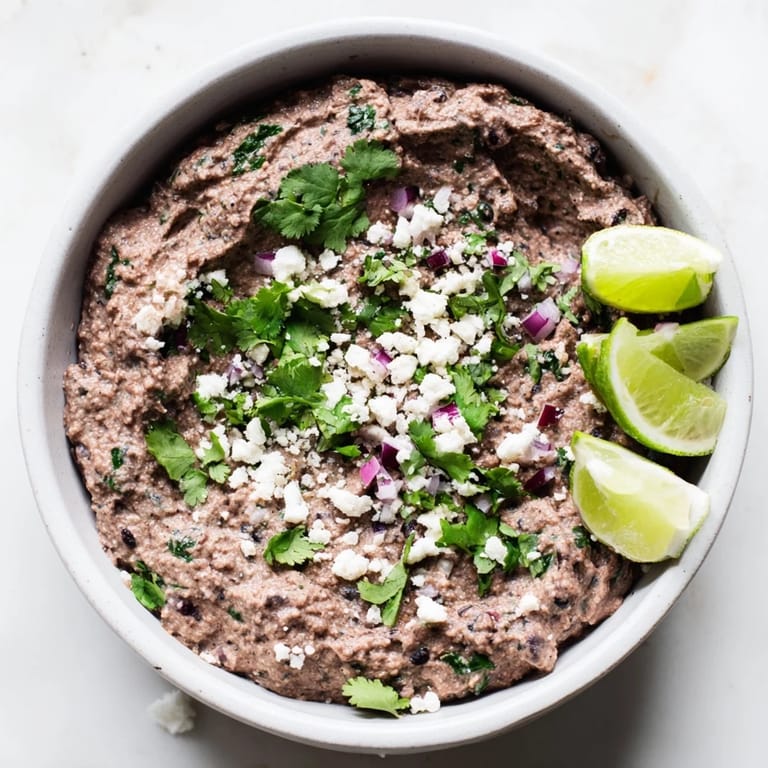 Spicy Black Bean Dip in a white bowl topped with cotija cheese and red onion, offering a zesty, vegan-friendly dip for gatherings.