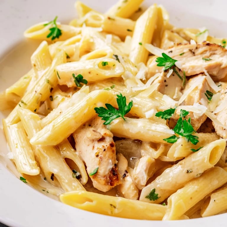 Steaming Roasted Garlic Chicken Penne served in a white bowl, garnished with extra Parmesan and a sprinkle of red pepper flakes beside a glass of wine.