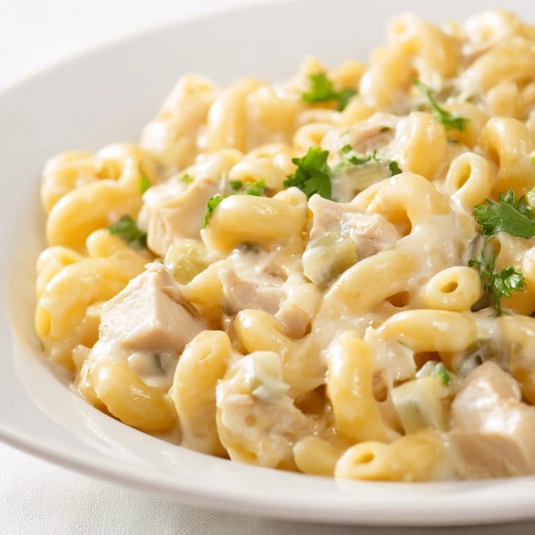 A serving spoon lifts creamy Green Chili Chicken Mac from a skillet, showing tender chicken, chiles, and melty Monterey Jack.