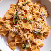 Creamy tomato basil bowtie pasta twirls on a fork with melted Parmesan and fresh herbs, perfect for a comforting weeknight dinner.