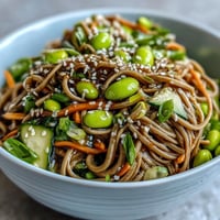 Soba Noodle Bowl with crisp cucumber, carrots, and edamame, drizzled with sesame dressing for a light meal.