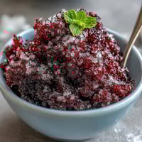 Bright red Black Currant Granita is shaved into fluffy ice crystals in a chilled glass bowl, ready to enjoy.