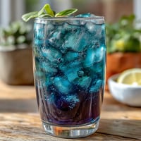 A vibrant glass of color-changing butterfly pea flower lemonade with ice and lemon slices.